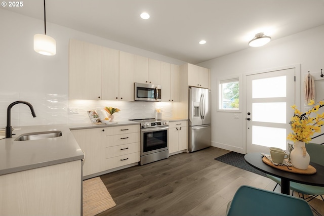 kitchen featuring pendant lighting, stainless steel appliances, decorative backsplash, dark wood-type flooring, and a sink