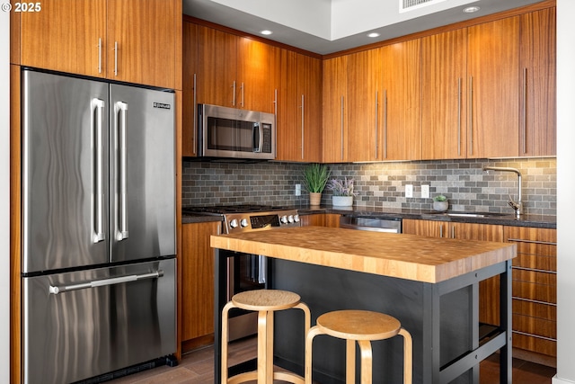 323 NW 13th Ave Unit 404, Portland, OR 97209 - kitchen featuring appliances with stainless steel finishes, wooden counters, brown cabinetry, backsplash, and a breakfast bar area