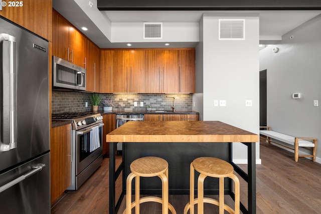 323 NW 13th Ave Unit 404, Portland, OR 97209 - kitchen featuring appliances with stainless steel finishes, brown cabinetry, dark wood-type flooring, a breakfast bar, and tasteful backsplash