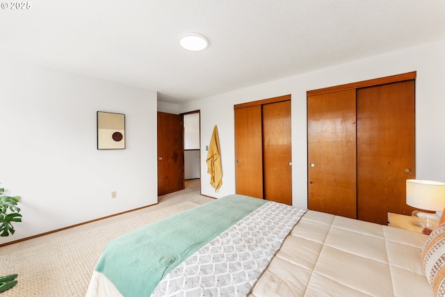 bedroom featuring baseboards, light colored carpet, and two closets