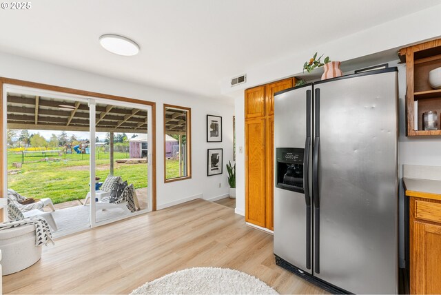kitchen with stainless steel fridge, light countertops, visible vents, brown cabinets, and light wood finished floors