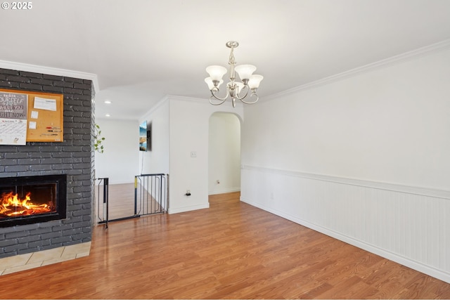 unfurnished dining area featuring an inviting chandelier, arched walkways, crown molding, and wood finished floors