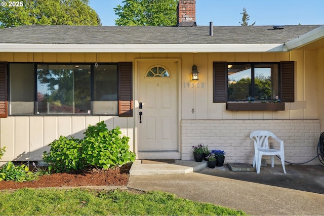 doorway to property featuring board and batten siding, a shingled roof, a chimney, and brick siding