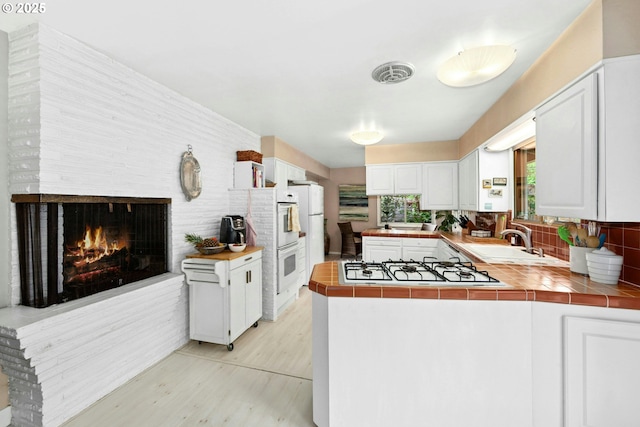 kitchen featuring a sink, tile counters, light wood-style flooring, white appliances, and a peninsula