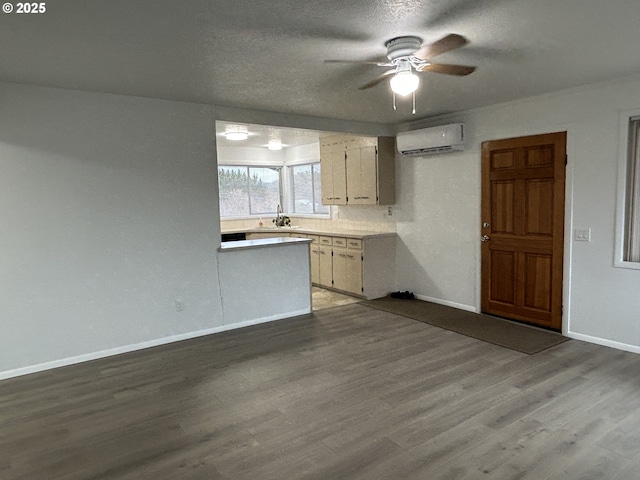 kitchen with light countertops, a wall mounted AC, a sink, wood finished floors, and baseboards