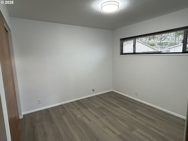 spare room featuring a textured ceiling, baseboards, and dark wood-type flooring