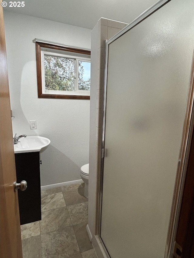 bathroom featuring a stall shower, toilet, vanity, and baseboards