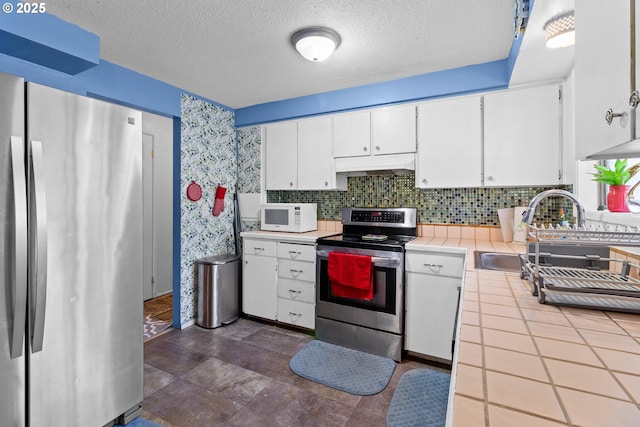 kitchen with appliances with stainless steel finishes, white cabinetry, sink, backsplash, and tile countertops