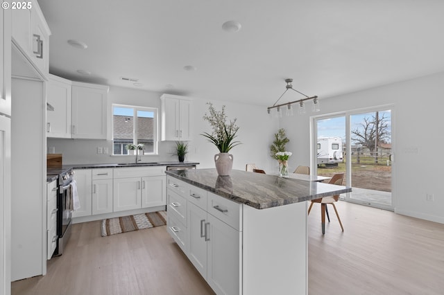 kitchen with white cabinetry, stainless steel range with electric cooktop, dark stone counters, a center island, and light hardwood / wood-style flooring