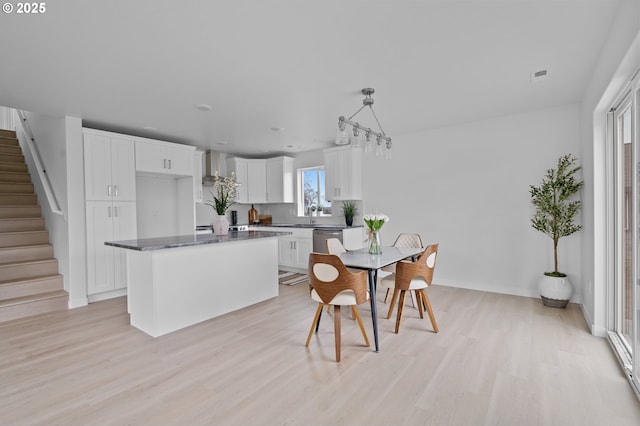 kitchen with sink, dishwasher, white cabinetry, a center island, and light wood-type flooring