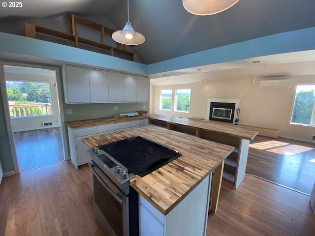 kitchen featuring wooden counters, stainless steel electric range oven, open floor plan, white cabinets, and high vaulted ceiling