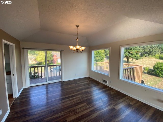 unfurnished room with healthy amount of natural light, a textured ceiling, dark wood-style flooring, a chandelier, and vaulted ceiling