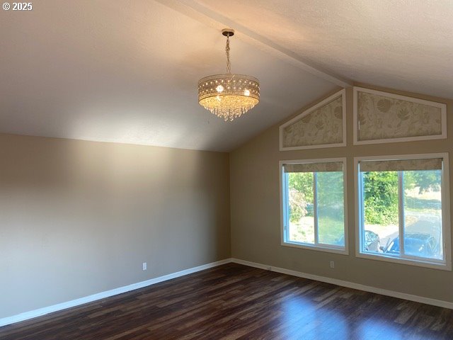 spare room featuring a chandelier, dark wood-style floors, lofted ceiling, baseboards, and a textured ceiling