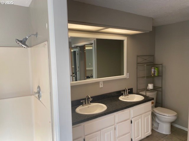 bathroom featuring tile patterned flooring, toilet, double vanity, and a shower