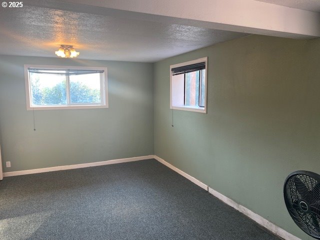 empty room with a textured ceiling, dark carpet, and baseboards