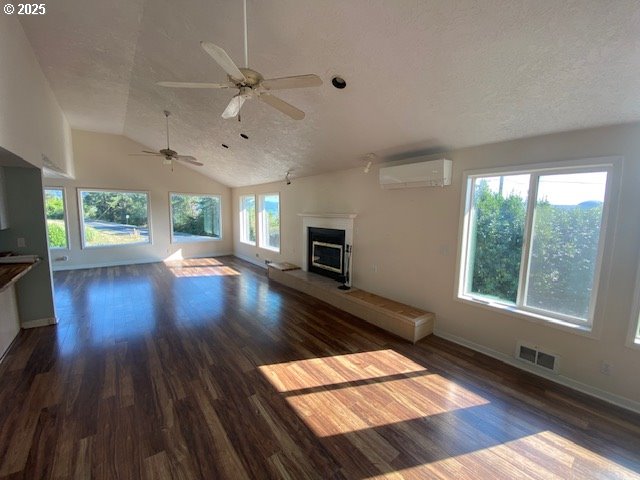 unfurnished living room with a wall unit AC, dark wood-type flooring, a fireplace with raised hearth, a textured ceiling, and lofted ceiling