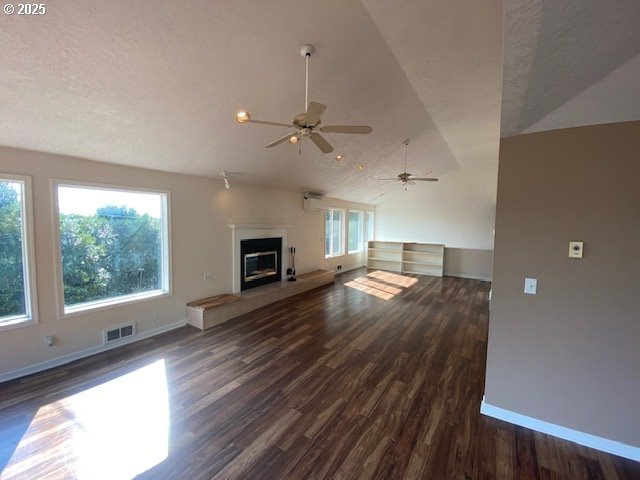unfurnished living room with dark wood-style floors, a ceiling fan, healthy amount of natural light, vaulted ceiling, and baseboards