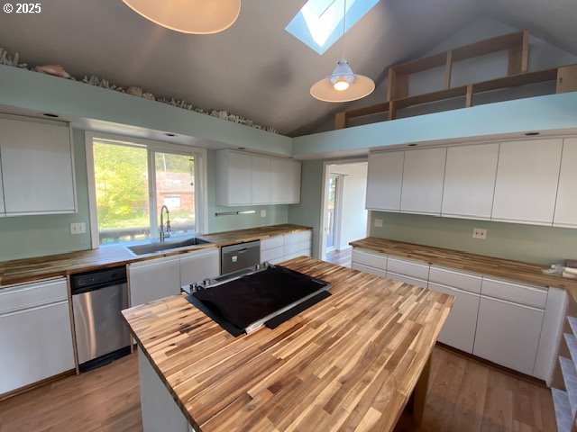 kitchen with wooden counters, a skylight, a sink, white cabinets, and high vaulted ceiling