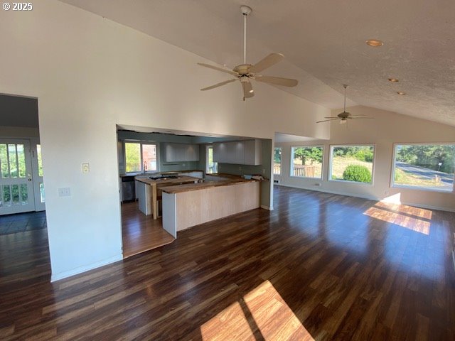 kitchen featuring open floor plan, dark wood finished floors, high vaulted ceiling, ceiling fan, and baseboards