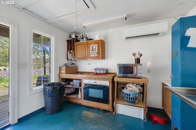 kitchen with stainless steel microwave, wall oven, a wall mounted AC, and finished concrete flooring