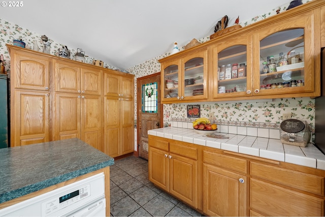 kitchen featuring light tile patterned flooring, wallpapered walls, glass insert cabinets, and lofted ceiling