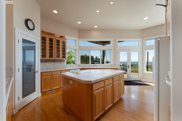 20700 SE Cherry Blossom Ln, Amity, OR 97101 - kitchen with tile countertops, light wood-style flooring, recessed lighting, freestanding refrigerator, and glass insert cabinets