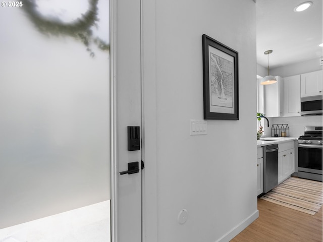 kitchen featuring sink, white cabinetry, light wood-type flooring, appliances with stainless steel finishes, and pendant lighting