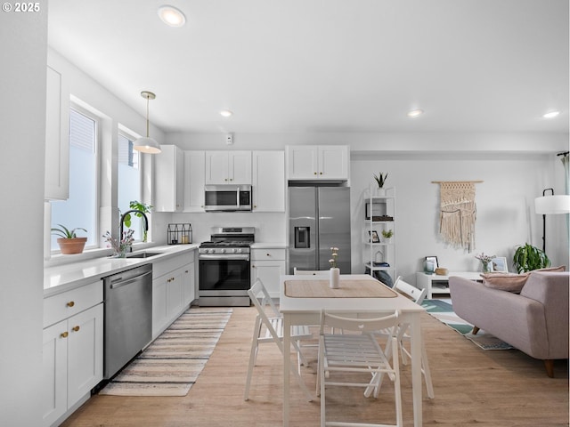 kitchen with appliances with stainless steel finishes, pendant lighting, white cabinetry, sink, and light wood-type flooring