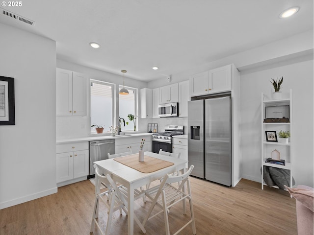 kitchen featuring sink, decorative light fixtures, light hardwood / wood-style flooring, appliances with stainless steel finishes, and white cabinets