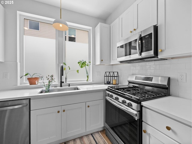 kitchen with appliances with stainless steel finishes, decorative light fixtures, white cabinetry, sink, and decorative backsplash