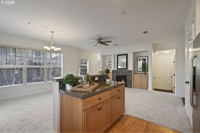 kitchen with pendant lighting, light colored carpet, a fireplace, and dark stone countertops