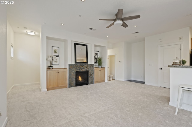 unfurnished living room with a tiled fireplace, light carpet, and ceiling fan