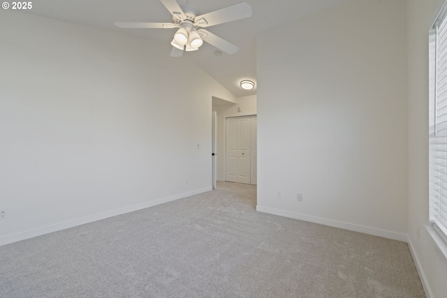 empty room with vaulted ceiling, a wealth of natural light, light colored carpet, and ceiling fan