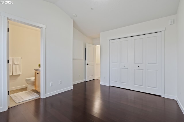 unfurnished bedroom with lofted ceiling, dark hardwood / wood-style flooring, ensuite bathroom, and a closet