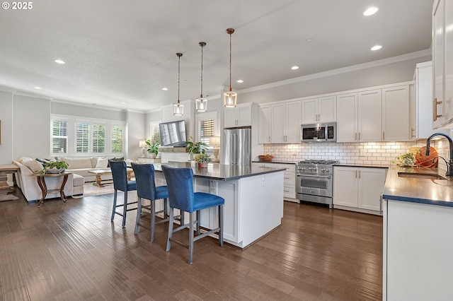 12339 SW Waterford Loop, Wilsonville, OR 97070 - kitchen featuring premium appliances, a sink, open floor plan, dark countertops, and crown molding