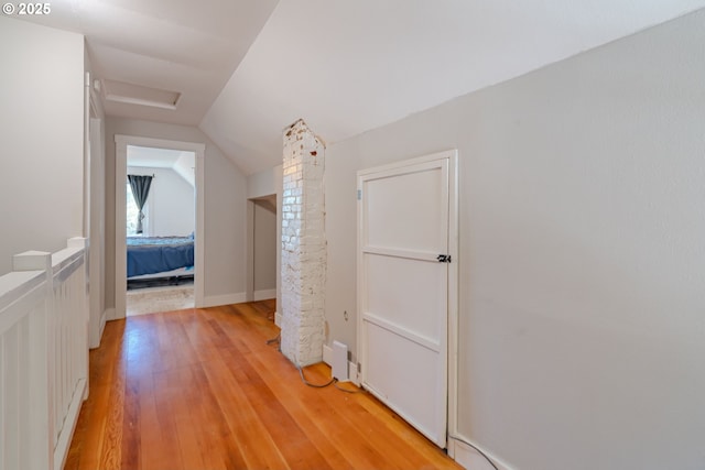 corridor with light wood-type flooring and vaulted ceiling