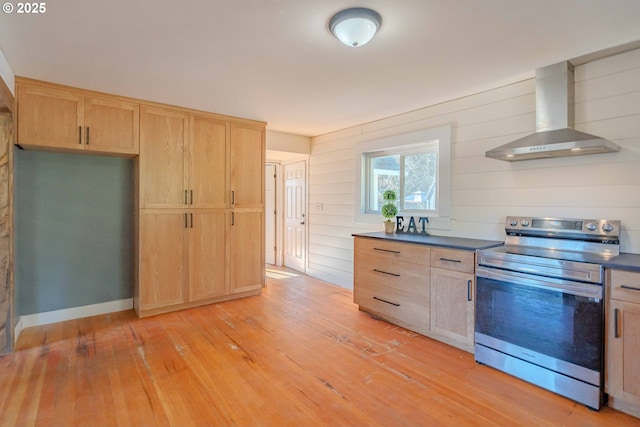 kitchen featuring light wood-type flooring, wood walls, light brown cabinetry, stainless steel range with electric stovetop, and wall chimney range hood