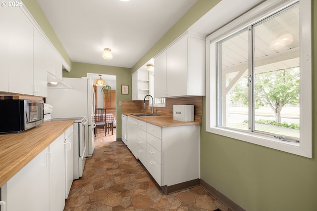 kitchen with a sink, white appliances, white cabinets, open shelves, and dark stone finish floors