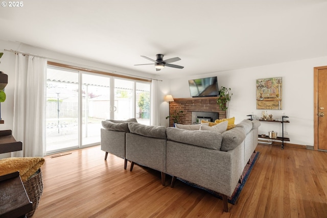 living area with light wood-type flooring, a ceiling fan, a fireplace, and baseboards