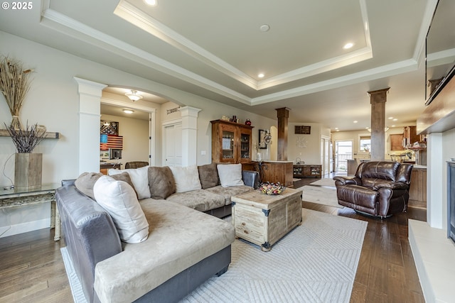 living area featuring arched walkways, a raised ceiling, ornate columns, and wood finished floors