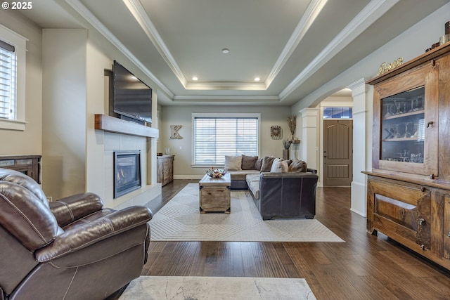 living room featuring arched walkways, a tray ceiling, dark wood-type flooring, and crown molding