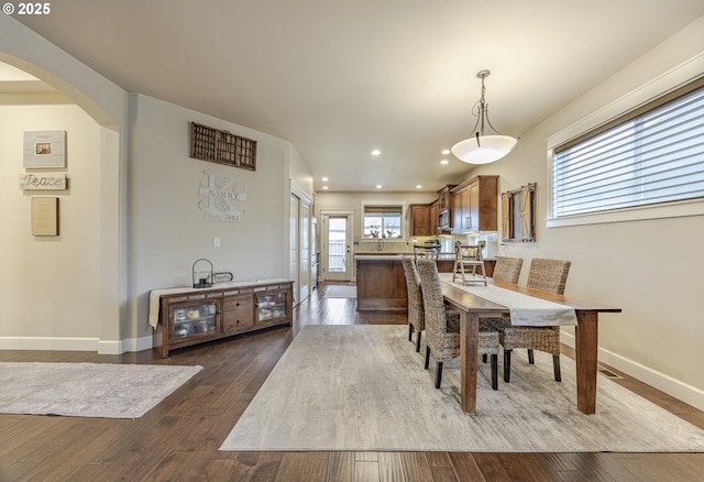 dining space featuring baseboards, arched walkways, wood finished floors, and recessed lighting