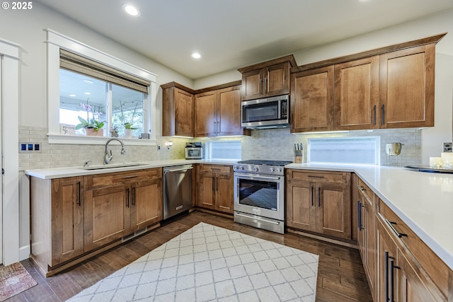 kitchen featuring brown cabinets, dark wood-style flooring, stainless steel appliances, light countertops, and a sink