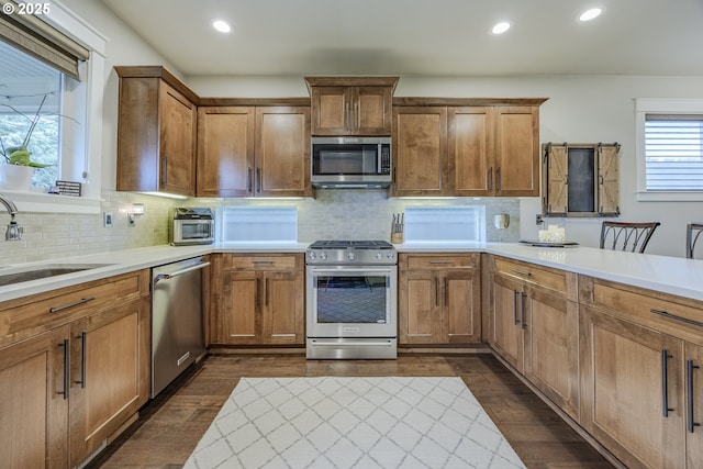 kitchen with stainless steel appliances, brown cabinetry, light countertops, and a sink