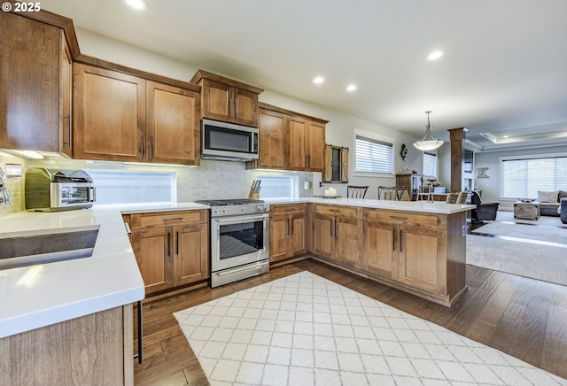 kitchen featuring brown cabinetry, hanging light fixtures, stainless steel appliances, light countertops, and a sink