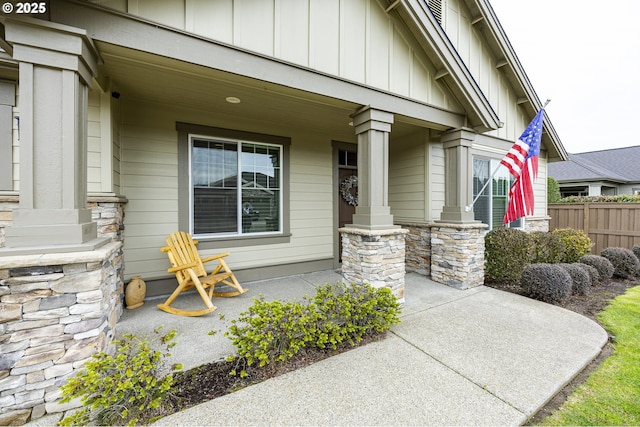 view of exterior entry featuring board and batten siding, covered porch, fence, and stone siding