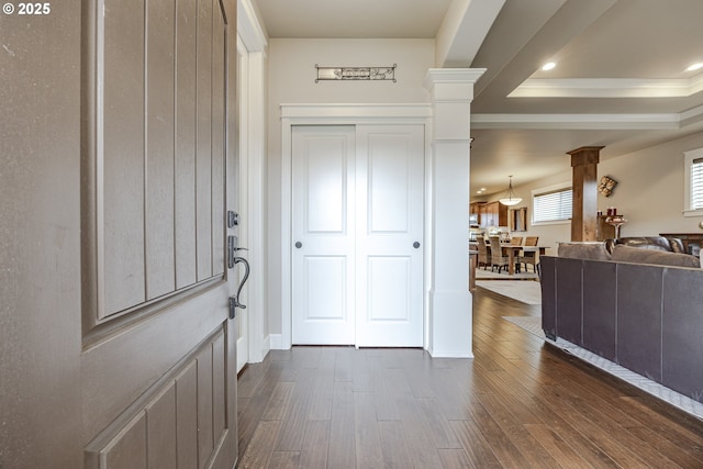 foyer entrance featuring a raised ceiling, dark wood finished floors, decorative columns, and crown molding