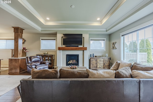 living room featuring a glass covered fireplace, a raised ceiling, and crown molding