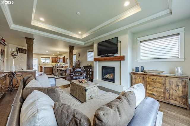 living room featuring a tray ceiling, light wood-style flooring, decorative columns, and a healthy amount of sunlight