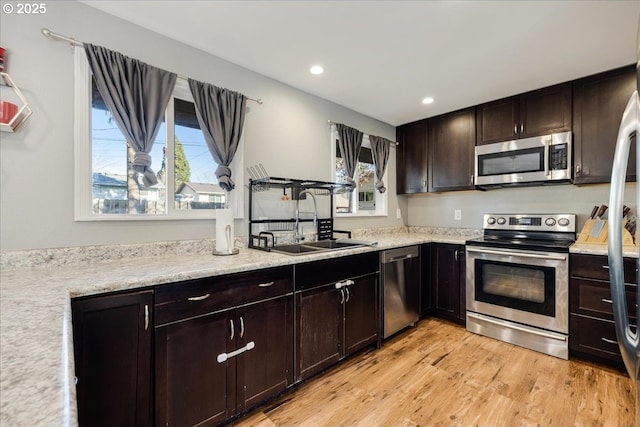 kitchen with appliances with stainless steel finishes, sink, dark brown cabinets, and light wood-type flooring